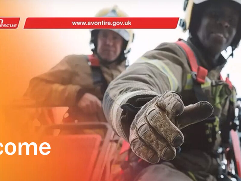 black firefighter holding out hand of help from crane with white firefighter behind looking at the camera