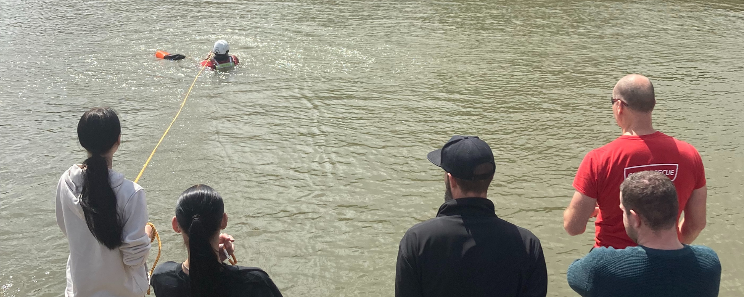 group of harbourside employees from local businesses practice throwing a throwline into the harbour to rescue a firefighter