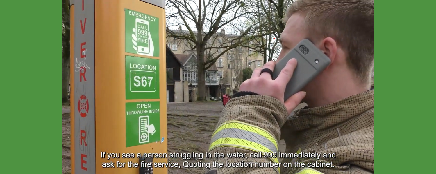 firefighter holding mobile phone calling 999 in front of river rescue cabinet box