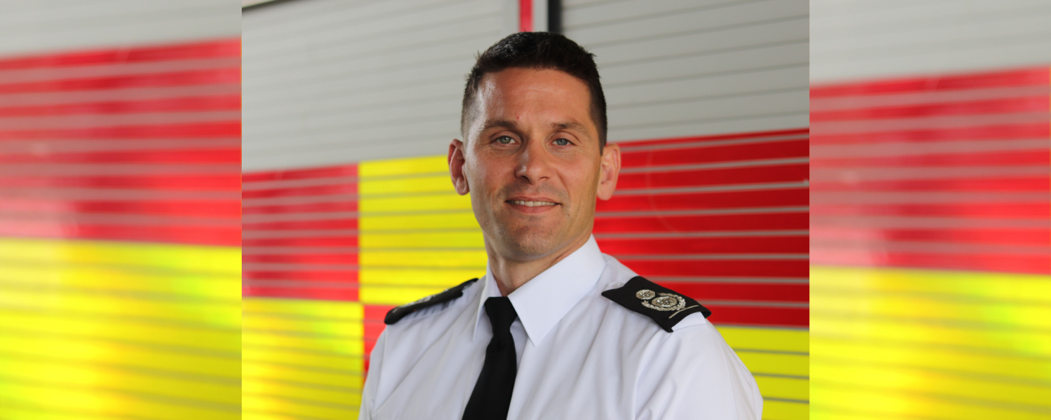 Chief Fire Officer Matt Cook stood in front of red and yellow fire engine.