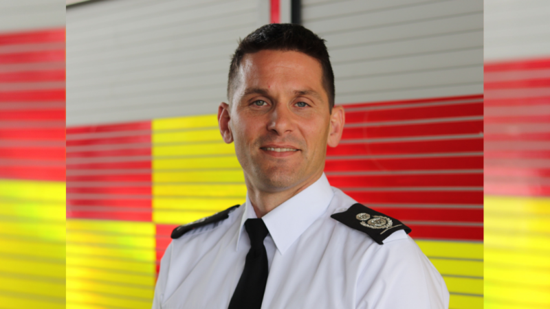 Chief Fire Officer Matt Cook stood in front of red and yellow fire engine.