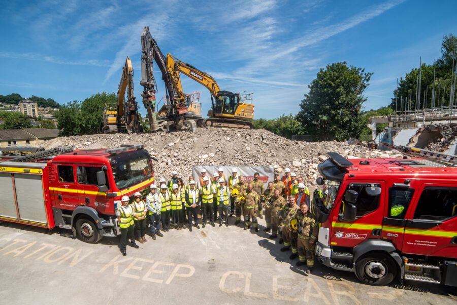 Staff from Avon Fire & Rescue Service and representatives from Willmott Dixon stand between two fire engines in front of the demolished fire station at Bath.