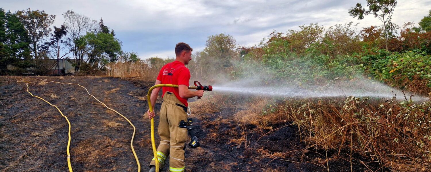 Firefighter stood in scorched field hosing down the shrubbery with water