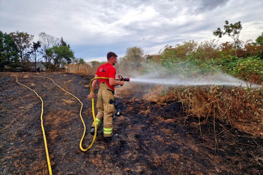 Firefighter stood in scorched field hosing down the shrubbery with water