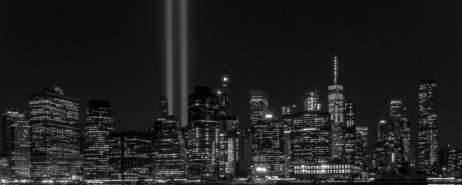 Image for 9/11, New York in black and white with lights shining up into the sky where the twin towers used to be.