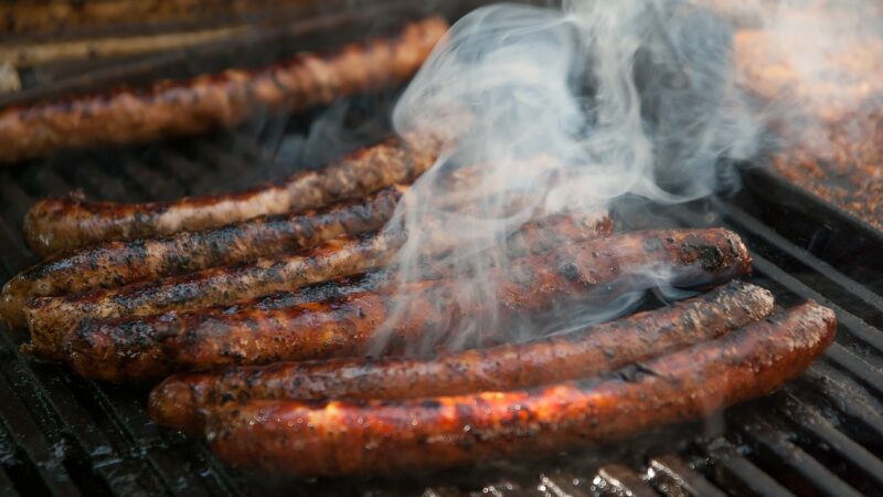 long chipolata sausages cooking on an outdoor grill