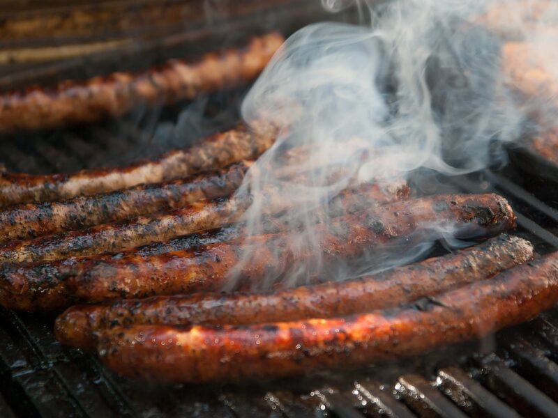 long chipolata sausages cooking on an outdoor grill