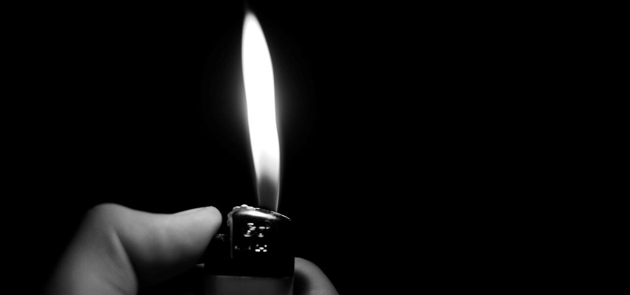 grayscale hand holding a gas lighter using the button to produce a flame