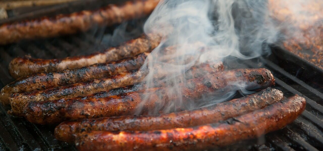 long chipolata sausages cooking on an outdoor grill